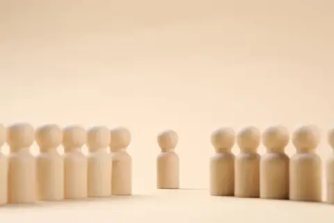 Un pupazzetto di legno si erge da solo, separato da un gruppo. Un simbolo di imparare a stare da soli, trovando forza nella propria individualità.