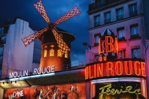 Le Moulin Rouge à Paris s'illumine la nuit, ses ailes de moulin rouge et jaune dansant sous le ciel sombre.