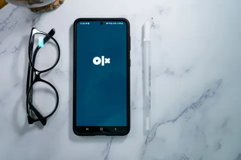 Telefon z aplikacją OLX, okulary i długopis na marmurowym tle. Dowiedz się, jak dodać ogłoszenie na OLX za darmo.