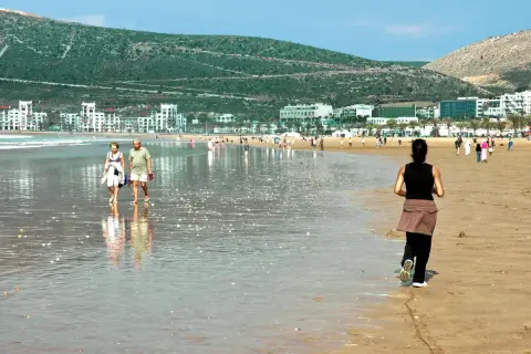 Spacerem po plaży w Maroku, w tle białe budynki i zielone wzgórza. Idealne wakacje.