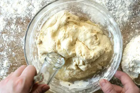 Dłoń dodaje olej do ciasta na roti w szklanej misce, otoczonej mąką.