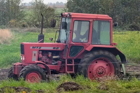 Czerwony traktor Belarus 820 pracuje na polu, za nim widać las.
