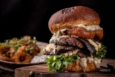Un généreux burger maison avec plusieurs steaks, fromage fondu et laitue fraîche, servi sur une planche en bois.