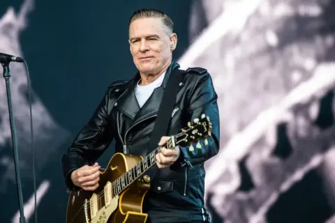 Bryan Adams w skórzanej kurtce gra na gitarze, przypominając klimat lata '69.