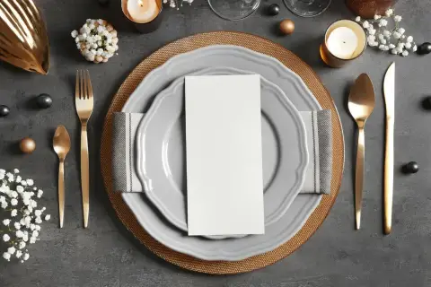 Elegancko ułożone sztućce: widelec po lewej, nóż i łyżka po prawej. Na talerzu biała kartka, idealna na menu.