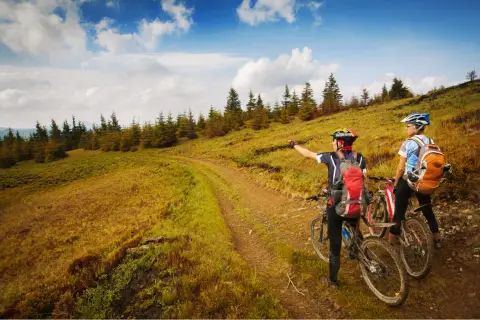 Dwóch rowerzystów na górskiej ścieżce, jeden wskazuje drogę. Piękna, słoneczna pogoda na przełęczy.