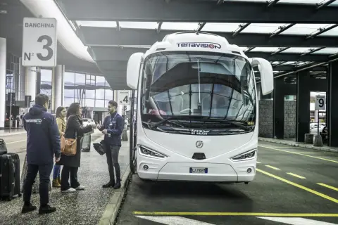 Autobus Terravision czeka na pasażerów na jednym z mediolan lotniska. Ludzie z bagażami rozmawiają z pracownikiem.