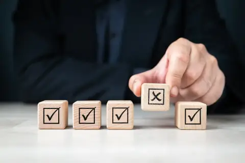 Dłoń kładzie kostkę z krzyżykiem na tle innych z zaznaczonymi ptaszkami. To symbol decyzji, jak w umowie przyrzeczonej.