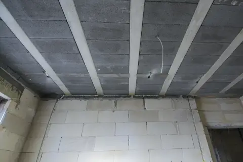 Widok na strop z pustaków i belek, gdzie widać przygotowania do tego, jak przeciągnąć kabel w suficie podwieszanym.