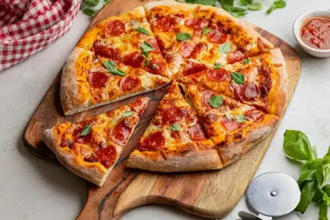 Pyszna pizza salami z ciągnącym serem i świeżą bazylią, pokrojona na kawałki, czeka na spróbowanie.
