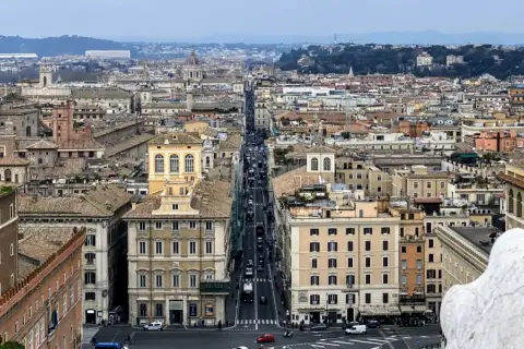 Vista aerea di Roma con traffico su Via del Corso. Edifici storici e tetti si estendono all'infinito.