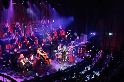 En orkester spelar på en scen i Stockholm, med en sångare i förgrunden. En levande revyupplevelse.