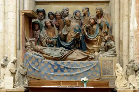 Kamienna rzeźba przedstawia scenę śmierci z wieloma postaciami. W centrum leży postać na łożu, otoczona przez żałobników. Scena ta, choć religijna, może budzić skojarzenia z bałwochwalstwem, gdyby skupiać się na formie, a nie treści.