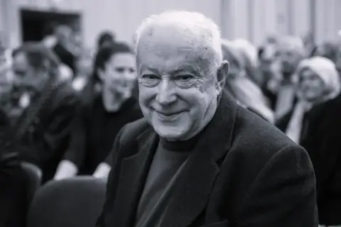 Uśmiechnięty starszy pan, być może syn Alicji Bobrowskiej, w otoczeniu ludzi.