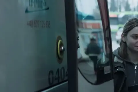Młoda kobieta patrzy w lustro autobusu, marząc, by jak najdalej stad.