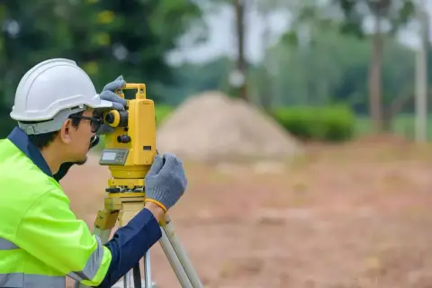 Geodeta w kasku i kamizelce odblaskowej pracuje z tachimetrem. Zastanawiasz się, ile kosztuje geodeta?