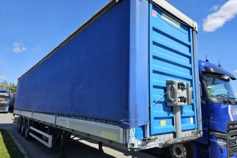 Naczepa tira z niebieską plandeką, gotowa do trasy. Standardowa ile szerokości ma naczepa tira, by pomieścić ładunek.