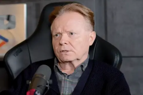 Michał Bajor siedzi w fotelu, przed mikrofonem, z nagrodą YouTube w tle.
