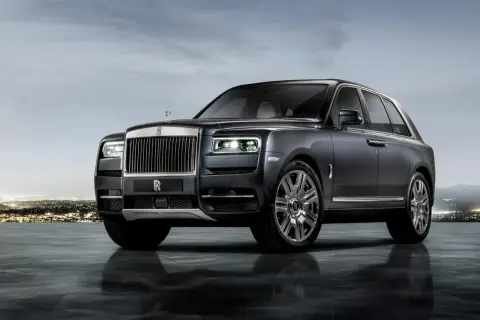 Elegancki Rolls-Royce SUV w ciemnym kolorze, lśniącym na tle nocnego miasta i gór.