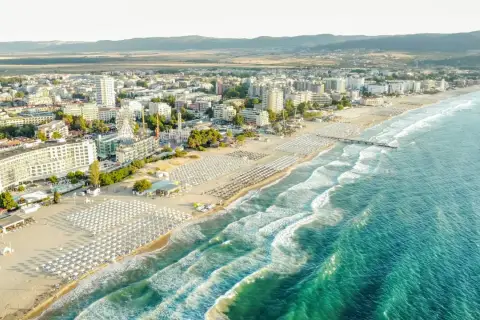 Słoneczna plaża w Bułgarii, morze z falami, rzędy leżaków i hotele tworzą wakacyjny krajobraz.