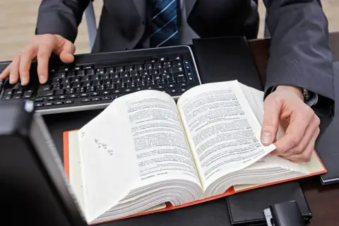 Mężczyzna w garniturze przegląda grubą księgę prawniczą, obok klawiatura.