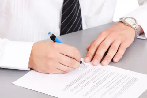Mężczyzna w białej koszuli i krawacie podpisuje dokument. Na nadgarstku ma zegarek. To ważny moment, gdy dodaje klauzulę CV po angielsku.