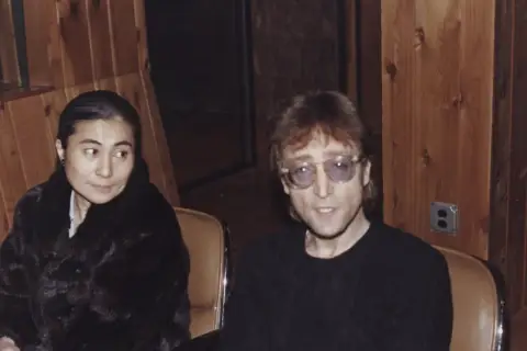 John Lennon i Yoko Ono siedzą w studiu. Yoko w czarnym futrze, John w okularach.