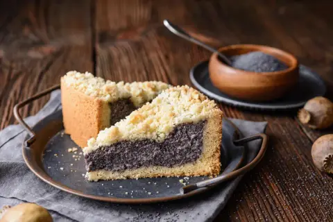 Zwei Stücke Mohnkuchen mit Puddingfüllung und Streuseln auf einem Teller, daneben eine Schale Mohnsamen.