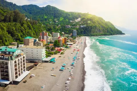 Widok na wybrzeże Gruzji, z zielonymi wzgórzami, kolorowymi budynkami i piaszczystą plażą nad turkusowym morzem.