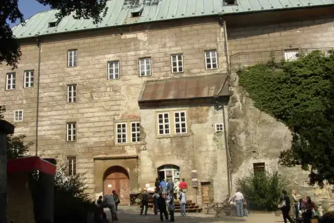 Kamienny zamek Houska z zielonym dachem i licznymi oknami, otoczony zielenią.