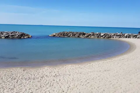 Spiaggia di Marina di Pisa con acque calme e dighe frangiflutti in pietra.