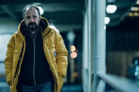 Mężczyzna w żółtej kurtce, zamyślony, idzie w stronę kamery. To kadr z filmu "Klangor", streszczenie szczegółowe tej sceny.