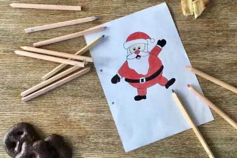 Buntstiftzeichnung eines lachenden Nikolaus auf Papier, umgeben von Buntstiften und Keksen.