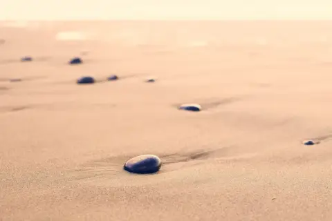 Kamienie na piaszczystej, dzikiej plaży, jak przebój Stana Borysa, tworzą ślady na piasku.