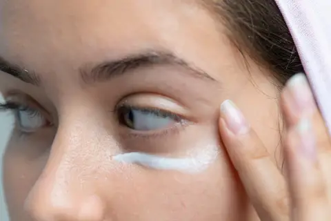Kobieta aplikuje maść arnikową pod oczy. Czytając opinie, warto wypróbować ten produkt na opuchliznę i cienie.