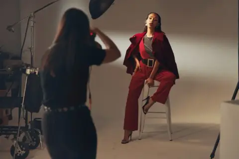 Sesja zdjęciowa w studio. Modelka w czerwonym stroju pozuje na stołku. Fotografka robi zdjęcie. Zastanawiasz się, ile zarabia fotograf?