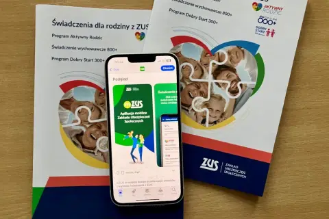 Aplikacja mZUS na telefonie pokazuje świadczenie wychowawcze 800+ dla rodziny. Ulotki ZUS informują o programach dla rodziców.