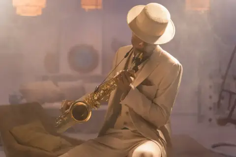 Mężczyzna w eleganckim garniturze i kapeluszu gra na saksofonie, tworząc niepowtarzalny styl w muzyce jazzowej.
