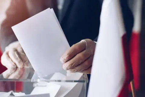 Ręka w rękawiczce wrzuca kartę do urny. Wybory, metoda Donty.