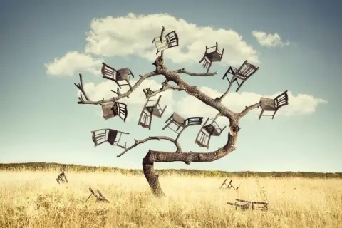 Drzewo pełne krzeseł, jakby wyrosło z nich, tworząc surrealistyczne omamy. Na trawiastym polu leżą połamane meble.