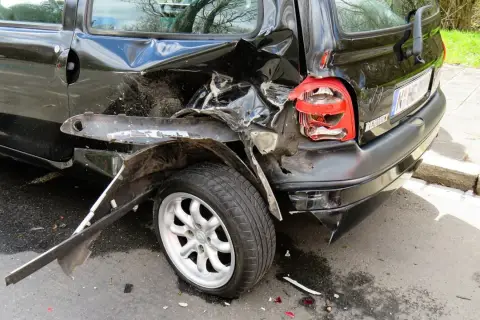Czarny samochód po wypadku, z pogiętym tyłem i rozbitym światłem. Jakby z sennika, czarny samochód w takim stanie budzi niepokój.