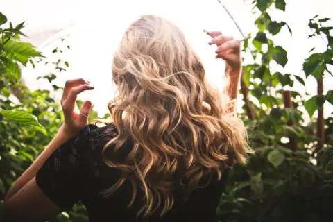 Kobieta z blond lokami w czarnej koronkowej bluzce na tle zieleni.
