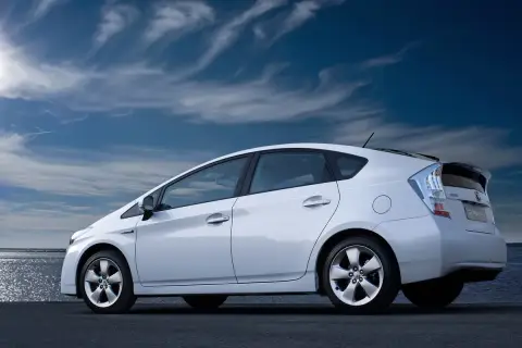 Biały Prius 3 zaparkowany nad wodą, pod błękitnym, chmurnym niebem.