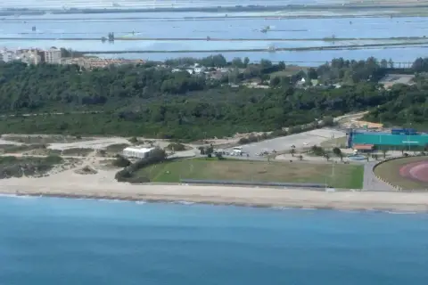 Vista aérea de la costa de El Saler, con el mar azul, la playa, dunas, vegetación, edificios y salinas al fondo.