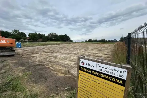 Tablica informacyjna budowy placu budowy z koparką w tle.
