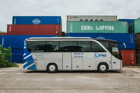 Autobus szkoleniowy z napisem "Linia Nauka Jazdy" na tle kontenerów. Sprawdź, jaka jest prawo jazdy kat d cena i zacznij kurs!