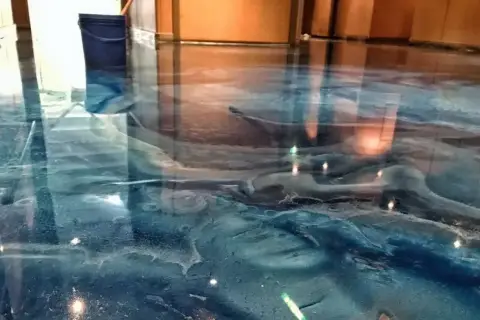 Błękitna żywica w garażu tworzy efekt fal oceanu. Widać niebieskie wiadro i odbicia światła.