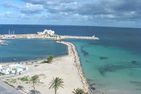 Piękna plaża i turkusowe morze w Tunezji. Październikowa pogoda sprzyja spacerom brzegiem, gdzie widać biały budynek i latarnię morską.