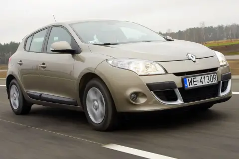 Złoty Megane 3 w ruchu drogowym, z widocznymi światłami i tablicą rejestracyjną WE 4130R.