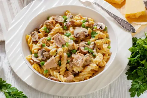 Makaron fusilli z tuńczykiem, groszkiem i pieczarkami w kremowym sosie, udekorowany natką pietruszki.